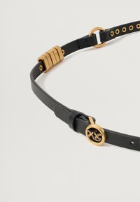 Cinto de couro preto com fivela circular dourada com motivo de pássaro, detalhes em ouro e furos ajustáveis com um acabamento texturizado.