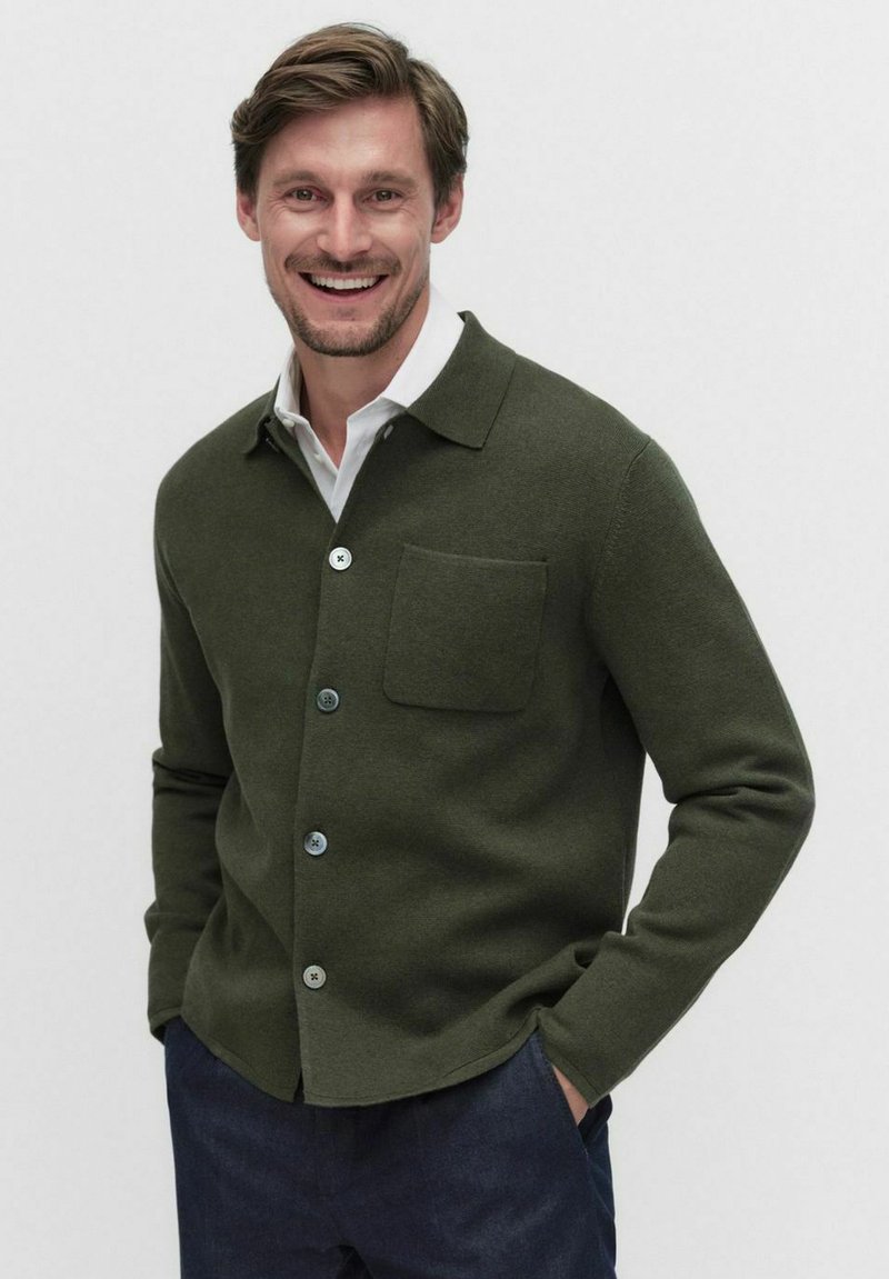 Olivgrön cardigan med knäppning framtill, spridd krage och en bröstficka. Mjuk textur och avslappnad passform. Blå knappar kompletterar designen.