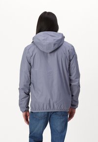 Veste légère grise avec capuche, poignets élastiques et ourlet. Le tissu semble lisse avec une finition mate, adapté à un usage décontracté.