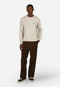 Sweater de malha bege claro com acabamento texturizado e decote redondo. Combinado com calças de cotone castanhas escuras e ténis preto e branco.