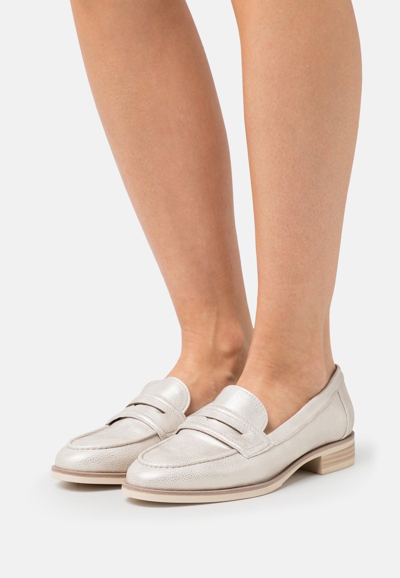 Mocassins en cuir argenté avec une finition texturée, présentant une sangle sur le devant, un petit talon carré et une semelle beige lisse.