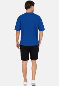 T-shirt bleu à manches courtes en coton, avec un col rond et un ourlet droit, associé à un short noir et des baskets blanches.