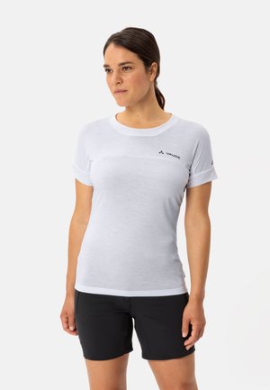 Chemise blanche à manches courtes avec un col rond, présentant une couture horizontale et un logo sur la poitrine gauche, associée à un short noir.
