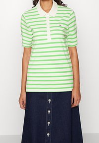 Woman wearing a short-sleeve green and white striped polo shirt with collar and a dark blue button-front skirt.