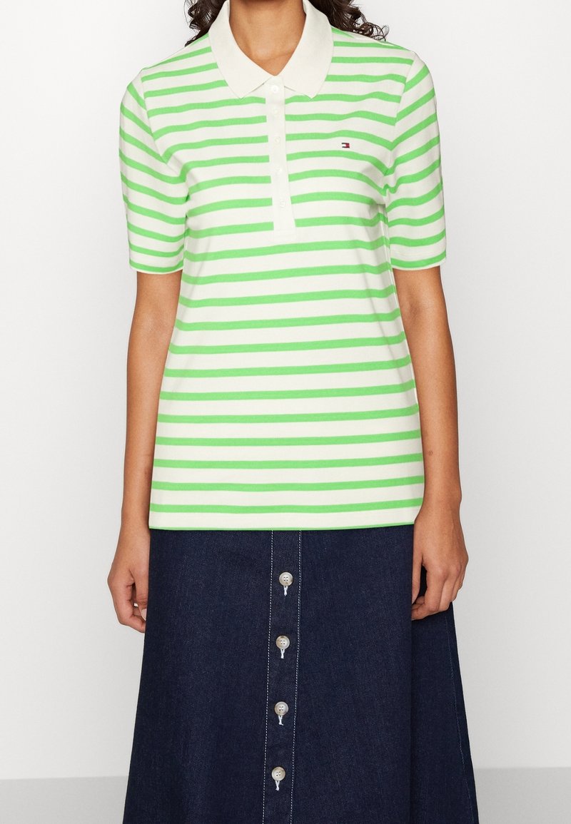 Woman wearing a short-sleeve green and white striped polo shirt with collar and a dark blue button-front skirt.