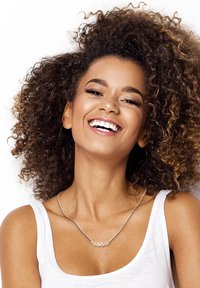 Sølv halskæde med bladdesign, båret på en bar kraveben, parret med en hvid ærmeløs top og indrammet af krøllet hår.