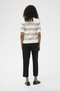 Woman standing facing away wearing a short-sleeve gray and white striped shirt, black cropped pants, and black loafers.