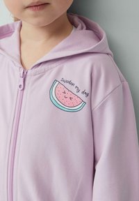 Lichtpaarse rits-hmok gemaakt van zachte stof, met een cartoonachtige watermeloenafbeelding en de tekst "sweeten my day" op de linkerborst.