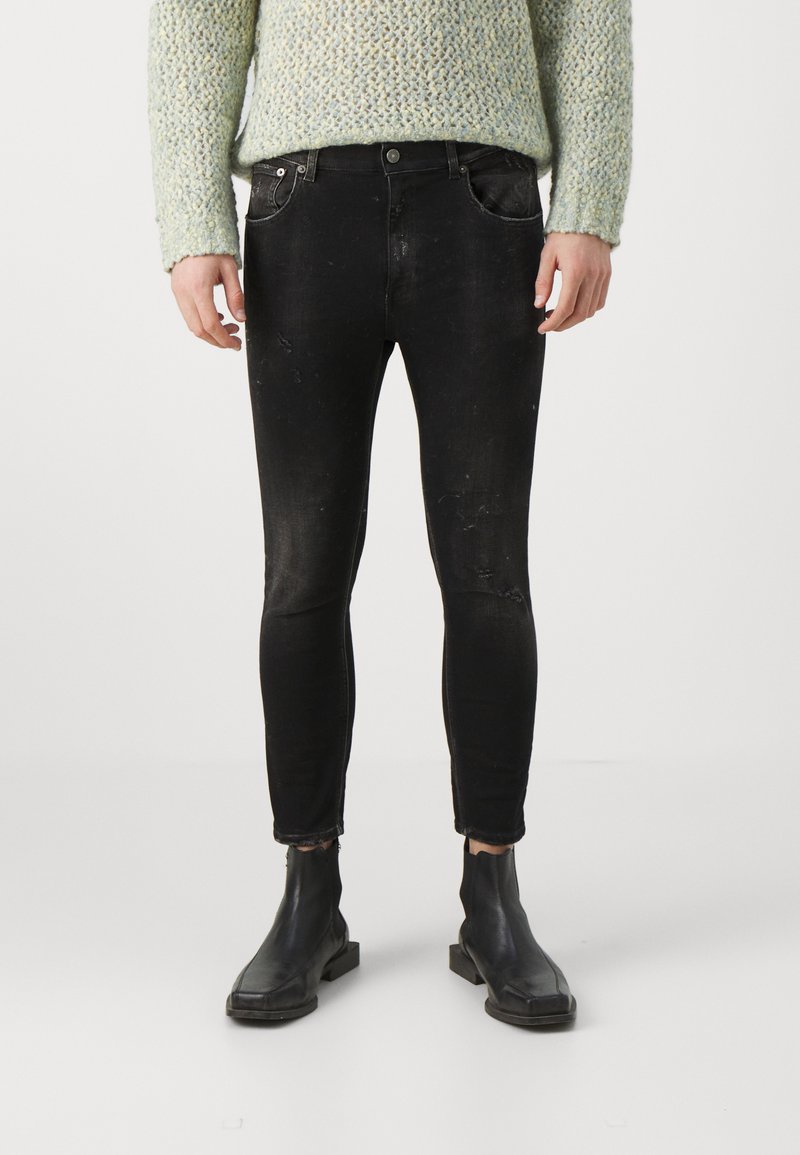 Jeans skinny neri con un finish rovinato, dotati di tasche anteriori, una cintura con passanti per la cintura e una vestibilità slim, abbinati a stivali neri alla caviglia.