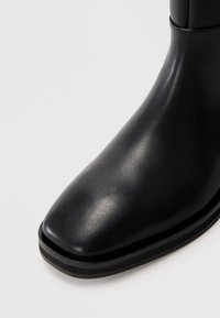Black leather ankle boot with a square toe, smooth surface, minimalistic design, and a sturdy, slightly raised black sole.