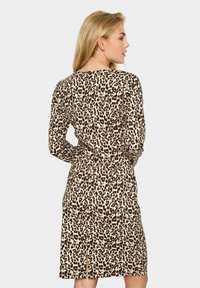 Haljina s uzorkom životinja koja ima bež pozadinu s crnim i smeškim leopard mrljama. Dugi rukavi i prorez na leđima za lakše kretanje.