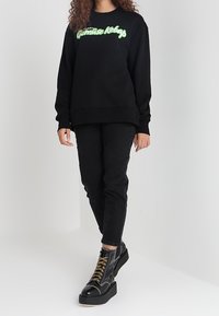 Black sweatshirt with green graphic text, paired with black skinny jeans and chunky black platform boots with gold laces. Simple design.