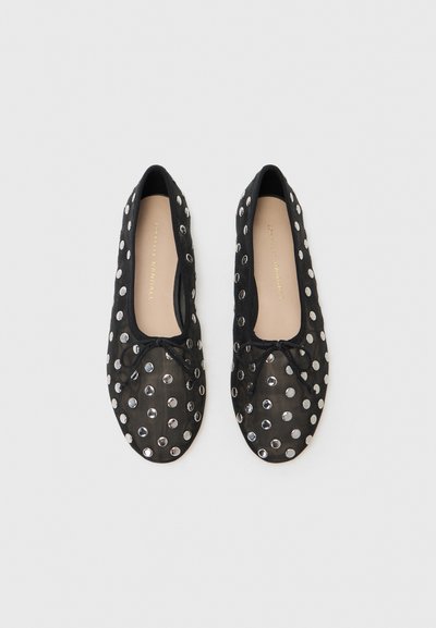 Ballerines noires en tissu mesh, ornées de clous métalliques argentés et d'un détail en nœud. Forme de bout arrondi avec un intérieur doux.