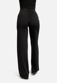 Mustad laia säärega püksid, mis on valmistatud siledast kangast, kõrge vöökohaga ja puhta äärega. Tagantpoolt näitab lõige kohandatud istuvust.