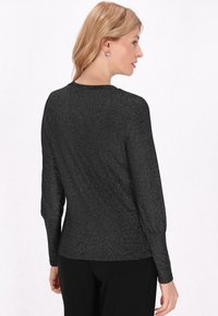 Fekete, hosszú ujjú felső, textúrált, csillogó felülettel. Kerek nyakkivágással és testhezálló ujjakkal rendelkezik, fekete nadrággal párosítva.