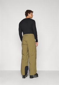 Pantalons de neige en tissu olive avec une coupe ample ; dotés d'un patch contrastant bleu marine au bas de la jambe et d'un logo sur le côté.