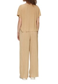 Lichtbeige tweedelig outfit met een geplooide, loszittende top en een brede broek, beide van een zachte, gestructureerde stof.