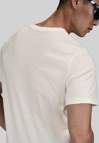 Camiseta de algodón beige con cuello redondo y mangas cortas, con una textura lisa y un diseño minimalista.