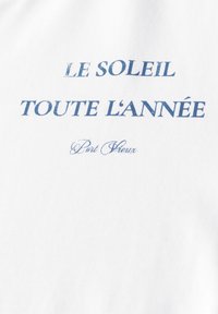 Valkoinen puuvillapaita, jossa on sinisellä painettu teksti: "LE SOLEIL TOUTE L’ANNÉE" ja "Port Grieux." Yksinkertainen muotoilu, jossa on sileä rakenne.