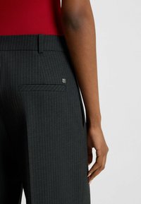 Pantaloni neri a righe sottili con una vestibilità slim, dotati di una tasca posteriore e un piccolo logo argentato vicino alla vita.