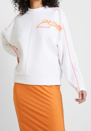 Felpa bianca con colletto alto, caratterizzata da dettagli rosa e un audace logo "PUMA" arancione. Abbinata a una gonna arancione per un contrasto.