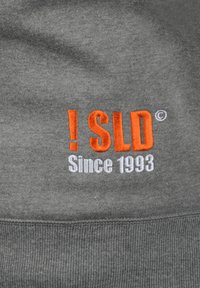 Sivi dukserica s izvezenim tekstom: "! SLD" u narančastoj boji i "Od 1993." u bijeloj boji. Ima rebrasti rub i mekan, teksturiran materijal.