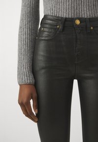 Jeans neri a vita alta con una texture liscia, hardware in argento e quattro tasche. Indossati con un maglione grigio a coste.