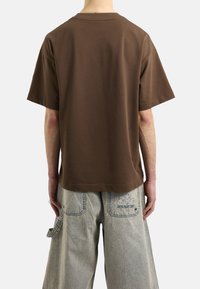 Brązowy T-shirt z krótkim rękawem o luźnym kroju, wykonany z miękkiej bawełny, z okrągłym dekoltem, w połączeniu z pasiastymi, luźnymi spodniami.