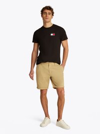T-shirt preta de gola redonda com um pequeno logótipo, combinada com calções beje de cintura subida e ténis brancos, apresentando um design suave e casual.