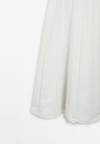 Jupe plissée légère en tissu gris pâle doux, avec une surface légèrement texturée et un ourlet brut pour un look décontracté.