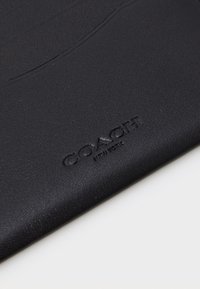 Black leather wallet with embossed "COACH NEW YORK" logo, featuring a textured finish and minimalistic design.