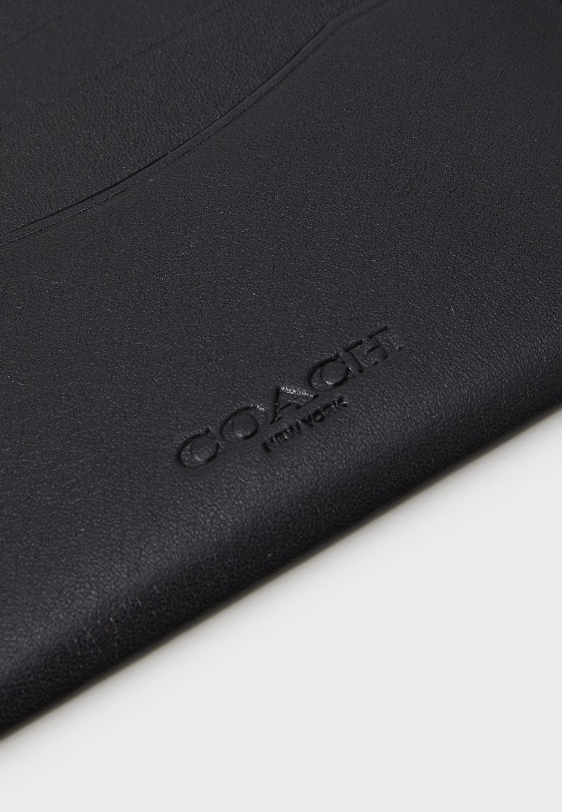 Svart läderplånbok med präglad "COACH NEW YORK"-logotyp, med en texturerad yta och minimalistisk design.