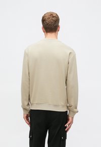 Beige pamut pulóver, kerek nyakkal, bordázott mandzsettákkal és aljjal. Laza fitet biztosít, és fekete cargo nadrággal van párosítva.