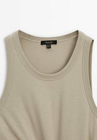 Débardeur beige sans manches avec encolure et emmanchures côtelées, en tissu doux, taille petite, étiquette indiquant la marque et l'origine.