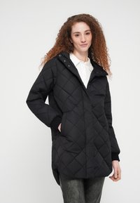 Μαύρο καπιτονέ μπουφάν με κουκούλα, με κλείσιμο με κουμπιά, πλαϊνές τσέπες και ριμπ μανσέτες. Λείο υλικό με ελαφρώς γυαλιστερό φινίρισμα.