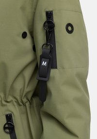 Groene waterdichte jas met een trekkoord in de taille, zwarte ritsen en een merklabel met een 'M'. Textiel met een gestructureerde stof en een gladde afwerking.