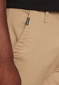 Bež hlače za moške iz strukture, z stransko žepom in črnim G-Star blagovno znamko na pasu.