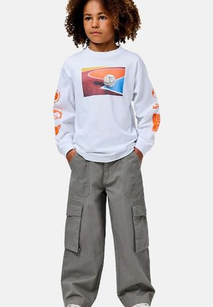 Weißes Langarmshirt mit mehrfarbigem Basketball-Print; kombiniert mit lockeren grauen Cargohosen mit Seitentaschen.