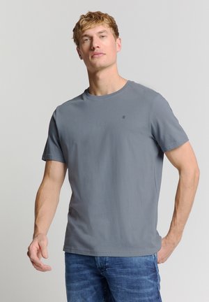 Grijze katoenen t-shirt met ronde hals en korte mouwen, met een subtiel logo detail op de borst. Gecombineerd met blauwe denim spijkerbroek.