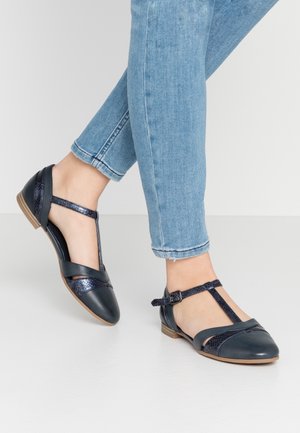 Navy blue T-strap flats with a combination of smooth and textured leather, rounded toe, and a low wooden heel. Adjustable ankle strap detail.