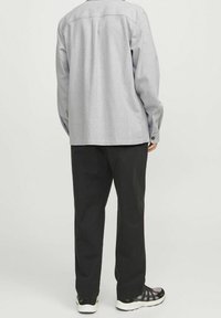 Šedá košile s knoflíky vpředu, rovného střihu, s dlouhými rukávy a zadním dílem, doplněná černými kalhotami a sportovní obuví.