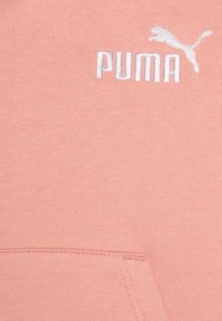 Roza dukserica s izvezenim bijelim Puma logom. Tkanina ima mekan, teksturiran završetak s vidljivim detaljima šivanja.