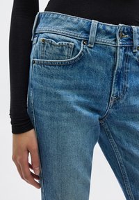 Μπλε τζιν παντελόνι με κλασική κοπή, που διαθέτει μπροστινή τσέπη, θηλιές για ζώνη και ραφές σε αντίθετο χρώμα. Το ύφασμα έχει ελαφρώς ξεθωριασμένο φινίρισμα.