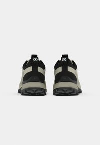 Zapatillas de trail negras y crema con parte superior texturizada, cuello acolchado y suela robusta con tacos pronunciados para una tracción mejorada.