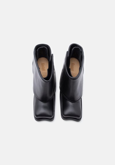 Μαύρα δερμάτινα μποτάκια αστραγάλου με τετράγωνες μύτες και μπεζ εσωτερικά, εμφανιζόμενα από επάνω σε λευκό φόντο.