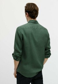 Vihreä pellavapaita, jossa on käärityt hihat, kauluksellinen pääntie ja kaareva helma. Pehmeä rakenne ja löysä istuvuus, esitetty takaapäin.