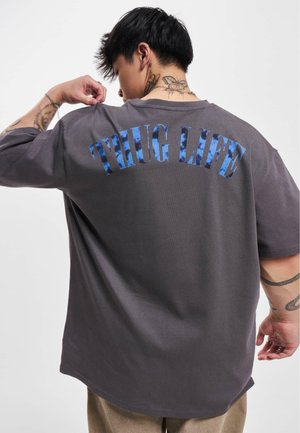 T-shirt oversize grigio con la scritta "THUG LIFE" in blu, realizzato in cotone morbido e con una vestibilità comoda.