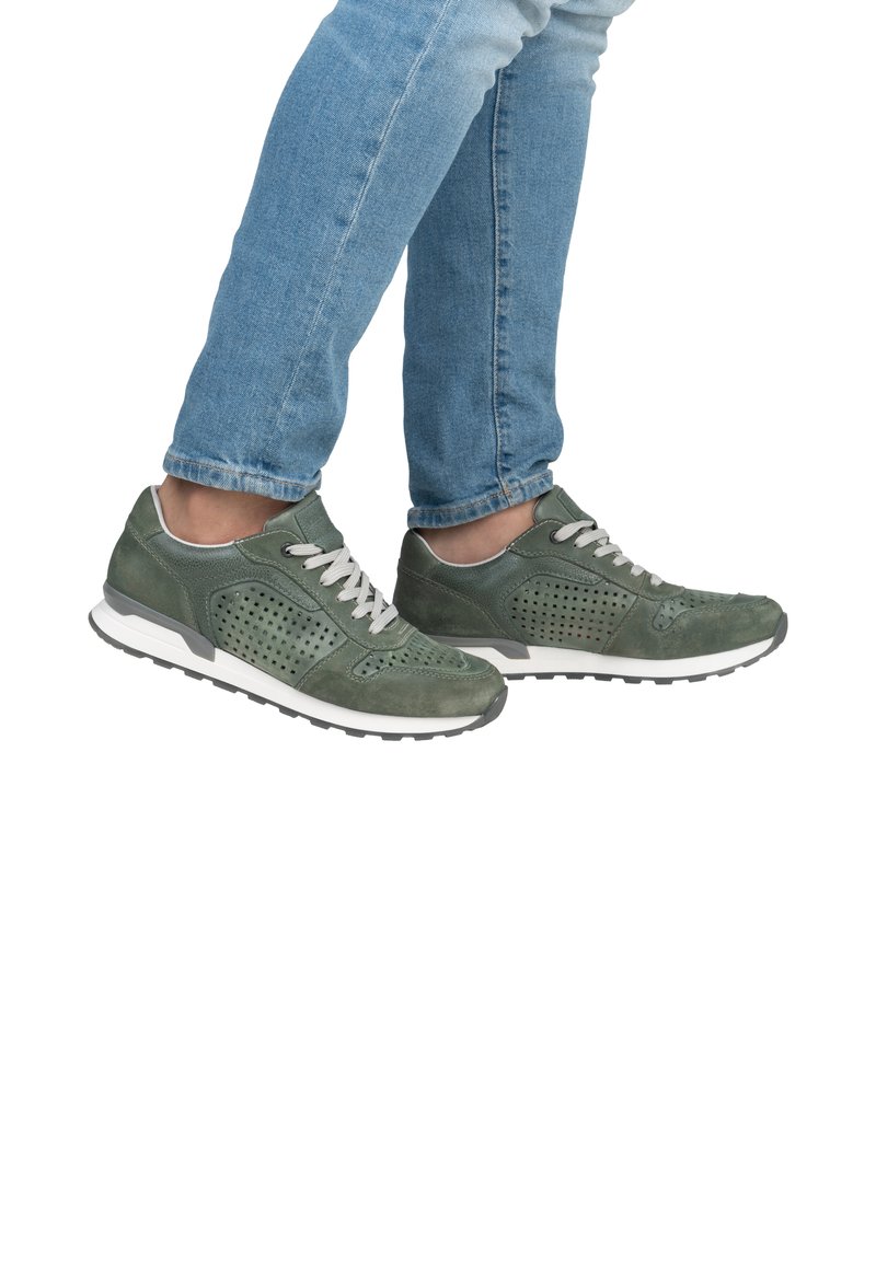 Grüne Wildleder-Sneaker mit durchbrochenem Design, grauen Akzenten, weißer Sohle und beigen Schnürsenkeln. Getragen mit hellblauen, eng anliegenden Jeans.