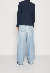 Marinblazer med en strukturerad design, kombinerad med ljusblå vida jeans. Denim har subtila blekningar och synliga bakfickor.