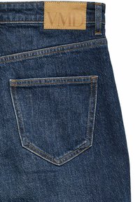 Jeans de mezclilla con un lavado azul oscuro, que presentan un parche de cuero etiquetado "VMD" y un único bolsillo trasero con detalles de costura en color naranja.